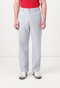 Pantalones de mezclilla azul claro con corte recto, con cierre de botón y trabillas para el cinturón, combinados con zapatillas blancas y grises.