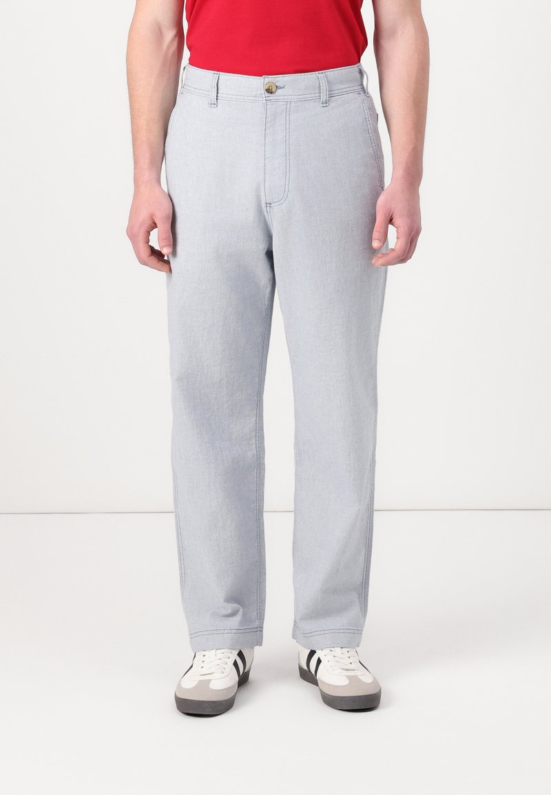 Pantalones de mezclilla azul claro con corte recto, con cierre de botón y trabillas para el cinturón, combinados con zapatillas blancas y grises.