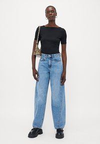 Črn prilegajoč se kratki top s kratkimi rokavi, v kombinaciji s svetlo modrimi širokimi jeans hlačami in masivnimi črnimi čevlji; model drži majhno torbico z zebrastepnim vzorcem.