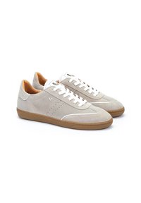 Zapatillas de ante gris claro con cordones blancos, suela de goma marrón y acentos perforados en los laterales. Presenta un diseño minimalista.