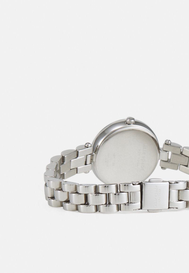 Orologio da polso in metallo argentato con bracciale a maglie e cassa rotonda sul retro, chiusura incisa con il nome del marchio, su sfondo bianco uniforme.