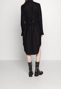 Svart klänning med vertikala ränder, långa ärmar, justerbart knyt i midjan och sidsprickor. Kombinerad med blanka svarta ankelkängor.