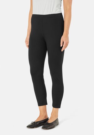 Zwarte leggings met een gladde textuur en een elastische tailleband, die toelopen bij de enkels. Gecombineerd met zwarte platte schoenen.