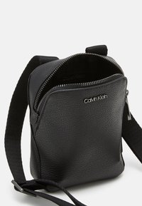 Borsa a tracolla nera in pelle con superficie texturizzata. Dotata di una chiusura con zip e una tracolla regolabile. Design piccolo e compatto.