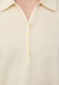 Polo shirt beige clair avec un col et une patte de boutonnage à cinq boutons. Texture de tissu lisse avec de subtils détails de couture.