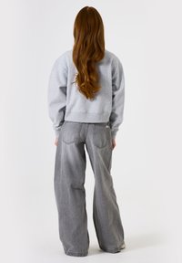 Sudadera gris corta con jeans gris de corte holgado. El conjunto presenta una textura suave y un diseño minimalista, enfatizando la comodidad.
