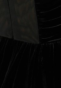 Svart sammetklänning med ett nätpanel, med inslag av samlad textur och slät yta. Designen inkluderar en figurnära överdel och en flödande kjol.