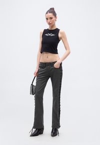 Μαύρο κοντό τοπ με λευκό γραφικό σχέδιο, συνδυασμένο με γκρι καμπανιαστά τζιν με δέσιμο στο πλάι. Αξεσουάρ περιλαμβάνουν μικρή τσάντα και μπότες με τακούνι.