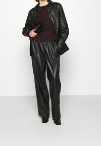 Černá kožená bunda přes burgundský svetr s pruhy zebry, v kombinaci s černými koženými kalhotami a špičatými černými botami, s černou psaníčkem.