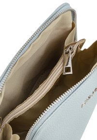 Interno di una borsa in ecopelle blu chiaro con rivestimento in tessuto beige, dotata di una tasca con zip e un dettaglio hardware della cerniera in argento.