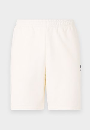 Shorts de color crema con una cinturilla elástica, hechos de tela suave, con un pequeño logo en la parte inferior de la pierna izquierda.