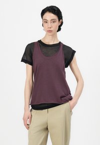 Diepe paarse V-hals tanktop gelaagd over een doorzichtige zwarte shirt met korte mouwen, gestyled met ontspannen beige broeken, die het casual ontwerp benadrukt.