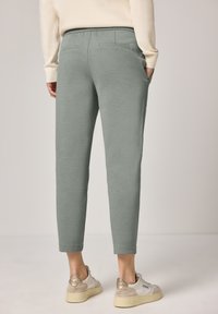 Jasnozielone spodnie dresowe o miękkiej fakturze, z dopasowanym krojem i dwoma tylnymi kieszeniami, w połączeniu z beżowymi trampkami.