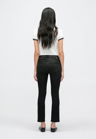 Fekete farmernadrág, karcsúsított fazonnal, középmagas derékkal és minimális varrási részletekkel. Fehér pólóval páros�ítva, hátulról látható.