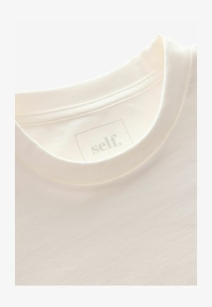 Balts, īsām piedurknēm T-krekls, kas izgatavots no mīkstas kokvilnas. Tam ir vienkārša apkakle ar smalku apdari, un iekšpusē ir uzlīme ar tekstu "self." pelēkā krāsā.