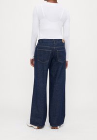 Breda ben mörk denimjeans med hög midja, med två bakfickor och kontrasterande sömmar. Bärs med en figurnära vit långärmad topp.