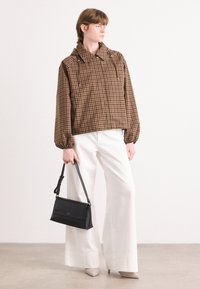 Braun kariertes, kurz geschnittenes Jackett mit Kapuze und elastischen Bündchen, kombiniert mit weißen weit geschnittenen Hosen und einer schwarzen Handtasche.
