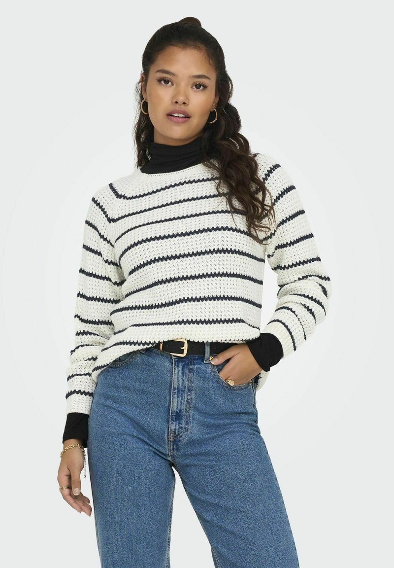 Knitted white sweater with black horizontal stripes, round neckline, long sleeves, paired with high-waisted blue jeans and a black belt.