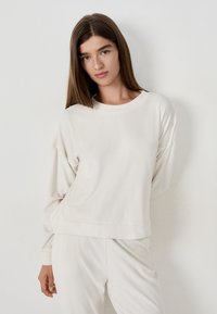Felpa beige chiaro con maniche lunghe, scollo rotondo e vestibilità rilassata, abbinata a pantaloni coordinati in tessuto morbido. Texture liscia.