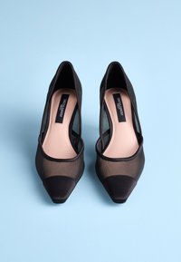 Black high-heeled shoes with mesh panels, pointed toe, and smooth texture; light nude footbed with logo; elegant design and classic shape.