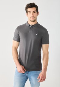 Grå polo-shirt med korte ærmer, lavet af et glat stof. Har en to-knaps placket og et lille hvidt fuglelogo på brystet.