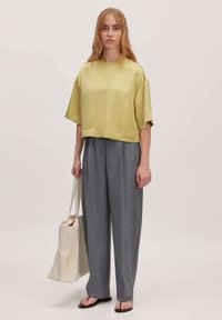 Hellgrünes Satin-Crop-Top mit kurzen Ärmeln, kombiniert mit grauen weiten Hosen und einer beigen Tragetasche. Glatte Texturen und lockerer Schnitt.