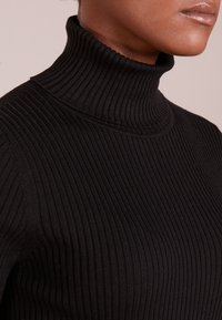 Schwarzer gerippter Rollkragensweater mit figurbetonter Passform, strukturiertem Stoff und hohem Kragen. Saubere Nähte sind sichtbar.