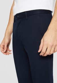 Navyblauwe broek van gladde stof, voorzien van een knoop- en ritssluiting, met een gestructureerde pasvorm en zijzakken.