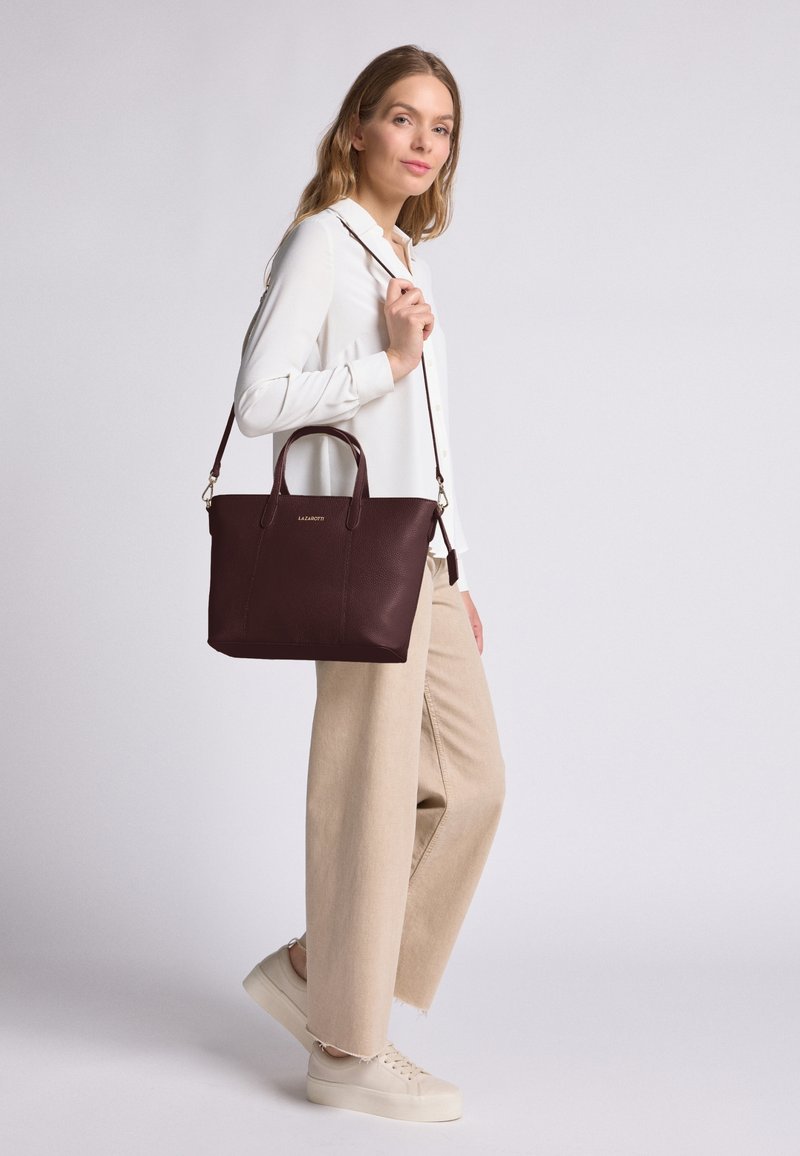 Bolso tote de cuero burdeos con dos asas superiores y una correa de hombro desmontable, con una superficie texturizada y un sutil detalle de logo.