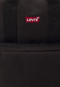 Sac à dos en tissu noir avec un logo Levi's rouge brodé, une poche zippée et un matériau synthétique durable.