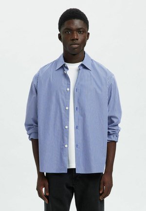 Blauw-wit gestreept shirt met een button-down kraag, lange mouwen en opgerolde manchetten, gelaagd over een wit T-shirt met ronde hals.