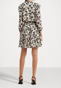 Blommig klänning med volangärmar i beige och svart, med en lager-på-lager kjol och genomskinlig överdel, kompletterad med svarta klacksandaler.