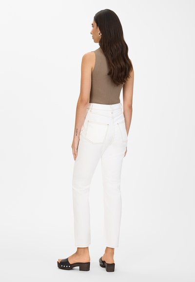 Jeans blancos de talle alto con bolsillos traseros visibles, combinados con una camiseta sin mangas de canalé marrón y zuecos negros con tacón, mostrados desde atrás.