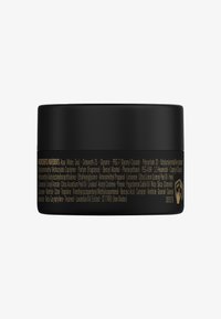 Svart cirkulär behållare med en jämn matt yta. Guldtext listar ingredienser på sidan. Platt lock med enkel design.