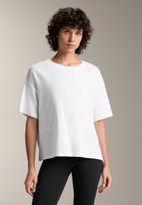 Vit oversized t-shirt i bomull med korta ärmar, rund halsringning och avslappnad passform, i kombination med svarta leggings. Minimalistisk design, mjuk textur.