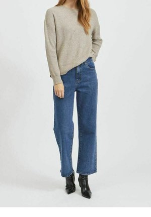 Maglione beige a maglia con vestibilità comoda, abbinato a jeans blu a gamba dritta e vita alta e stivaletti neri con punta a mandorla.