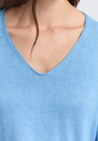 Jasnoniebieski top z dekoltem w serek, wykonany z miękkiego, lekkiego materiału; gładka tekstura z subtelnym połyskiem; posiada krótkie, swobodne rękawy i staranne szwy.