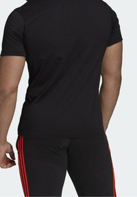 Mustat lyhythihaiset t-paidat, joita on yhdistetty mustiin housuihin, joissa on punaiset sivuviivat; pehmeä materiaali ja istuva malli, vähäinen brändäys.