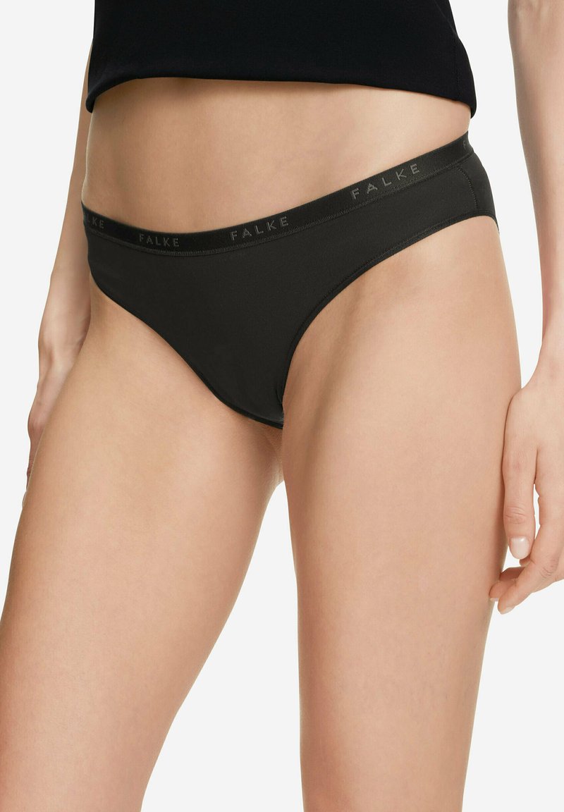 Kobieta nosząca czarne majtki o wysokim kroju z markowym paskiem, pokazana od talii do górnej części ud na białym tle.