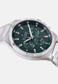 Montre à cadran vert avec bracelet en acier inoxydable argenté. Les caractéristiques incluent un affichage de la date, des indicateurs de jour et de grands repères horaires.