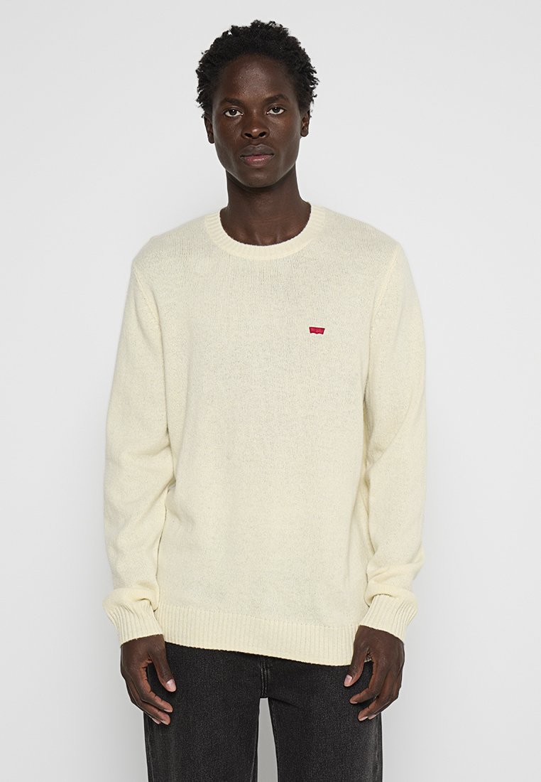 Maglione a maglia color crema con scollo rotondo, polsini e orlo a costine. Presenta un piccolo logo rosso sul lato sinistro del petto.