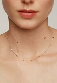 Collar de tono dorado con encantos en forma de estrella, cadena delicada, textura suave y acentos espaciados de manera uniforme, descansando sobre piel desnuda.