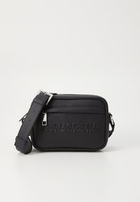 Borsa a tracolla nera in pelle con logo in rilievo, chiusura con zip, tracolla regolabile e superficie texturizzata. Forma compatta e rettangolare.