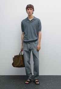 Grey short-sleeve polo with a textured pattern, paired with light denim jeans and brown leather sandals. Holds a brown tote bag.