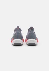 Gray athletic shoes with distinctive red accents. Features a textured upper, supportive heel counter, and a flexible sole design.