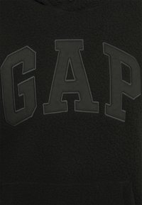 Tessuto nero con texture, caratterizzato da grandi lettere grigie scure "GAP" ricamate in un font bold e in stile block.