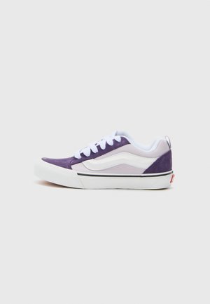 Baskets en suède violettes et blanches avec un design basse, présentant un bout arrondi, des lacets blancs et une bande noire le long de la semelle.