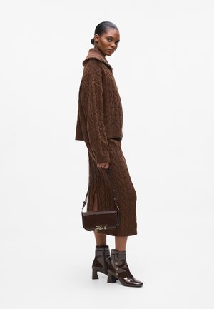 Brown knitted sweater with a hood and cable pattern, paired with a matching skirt. Glossy brown ankle boots and a small shoulder bag.