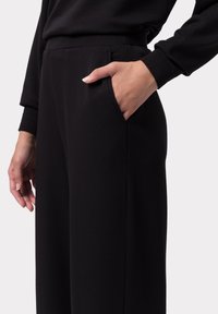 Pantalones negros de pierna ancha con una textura suave, que cuentan con un bolsillo lateral y una cinturilla ajustada. La tela parece suave y elástica.