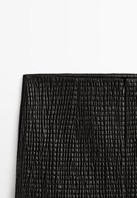 Jupe en cuir noir texturé avec des détails de coutures verticales et horizontales, présentée à plat sur un fond blanc.